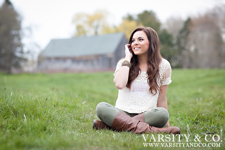 girl sitting in a field with a barn in the background senior picture